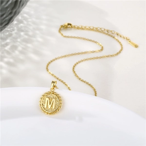 Close-up of gold round pendant with embossed letter M and beaded edge on link chain