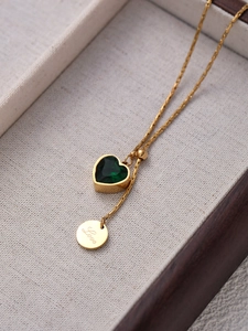 Dettaglio della collana dorata con gemma a cuore verde e ciondolo Love in scatola