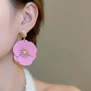 Boucles d'oreilles fleur rose et perle avec détails dorés portées par un mannequin