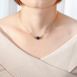 Detailed view of dainty gold choker with blue lapis lazuli bead on a model's neck