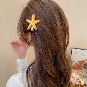 Détail de la pince à cheveux étoile de mer en raphia tissé avec diamant sur cheveux bouclés