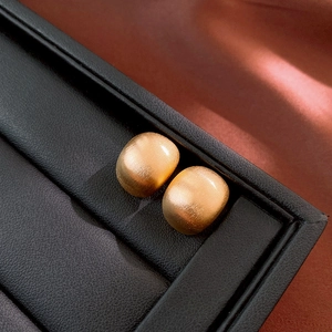 Gros plan sur des boucles d'oreilles carrées dorées avec texture brossée sur cuir