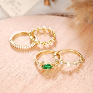 Detalle de cuatro anillos apilables dorados con piedra marquesa verde sobre madera