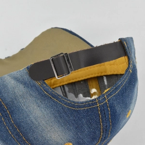 Detail of adjustable leather strap and metal buckle on blue washed denim baseball cap