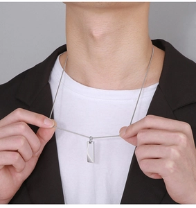 Close-up of a silver rectangular pendant on a snake chain worn by a male model