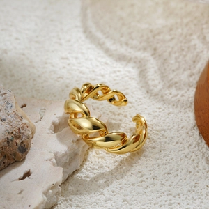 Detailed close-up of a twisted gold ring on natural sand and coral stone background