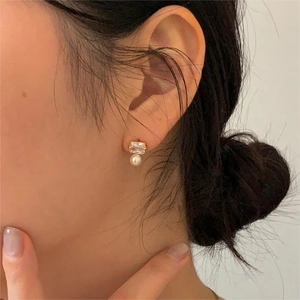 Detailed view of square cubic zirconia and pearl stud earring on model ear with gold plating