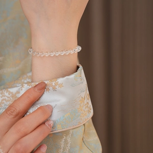 Close-up of faceted clear crystal bead bracelet worn with elegant embroidered clothing