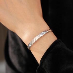 Détail du bracelet argenté à texture matelassée croisée avec zircone au poignet
