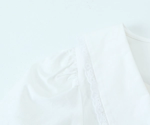 Dettaglio di abito bianco in popeline con colletto in pizzo e maniche a sbuffo
