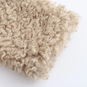 Close-up of high-quality light beige curly faux fur fleece texture with soft plush fibers