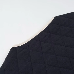 Detailed close-up of black quilted diamond fabric with contrast beige binding on neckline