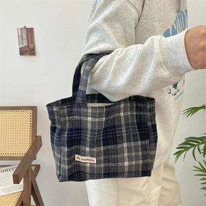 Close-up of vintage plaid tote bag with textile label against a cozy interior backdrop