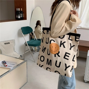 Detail einer großen cremefarbenen Segeltuch-Tasche mit orangefarbenem Smiley und schwarzen Buchstaben