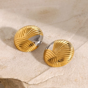 Macro view of 18k gold and silver irregular ribbed earrings on a beige stone surface