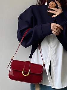 Close-up of a burgundy patent leather shoulder bag with a gold horseshoe buckle detail