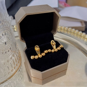 Macro view of golden bead stud earrings displayed in a luxury brown hexagonal jewelry box