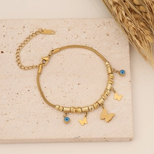 Golden stainless steel butterfly and evil eye bead necklace displayed on stone with wheat