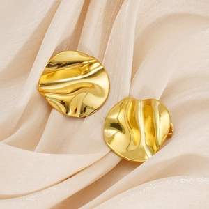 Détail de boucles d'oreilles dorées plissées avec texture ondulée sur un tissu en soie