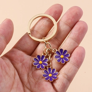 Golden keychain with three purple enamel daisy flower pendants held in hand