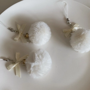 Macro detail of three fluffy white plush ball charms with cream satin bows in a ceramic dish