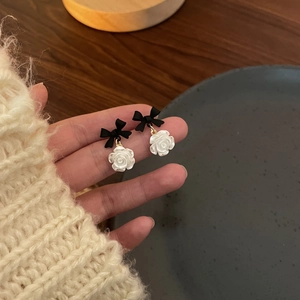 Detailed view of matte black bow earrings with white 3D resin roses on gold metal rings