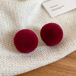 Macro shot of red flocked ball stud earrings on a beige knit fabric and wood background