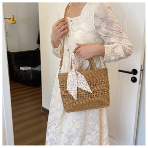 Detail of straw crossbody bag with floral scarf handle in natural indoor setting