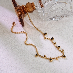 Detail of gold beaded necklace with black gemstones on a minimalist white background