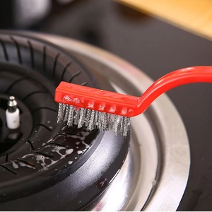 Strong metal cleaning brush with red handle scrubbing grime off a gas stove burner