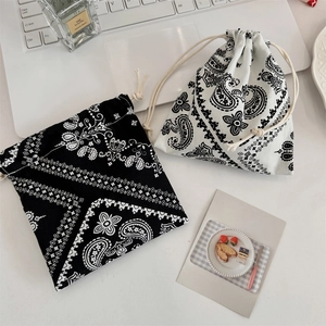 Detailed view of paisley drawstring pouches in black and white with lifestyle props