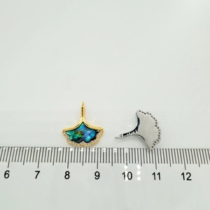 Macro detail of a 18k gold-plated ginkgo leaf pendant with abalone shell inlay and size scale