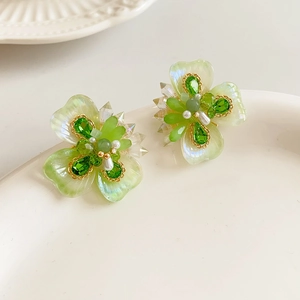 Détail macro de boucles d'oreilles fleurs avec cristaux verts et perles blanches