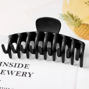 Detail of a large black glossy hair claw clip with dense teeth on a lifestyle background