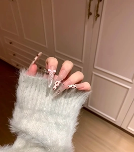 Gros plan sur ongles stiletto avec motif léopard, nœuds blancs et strass brillants