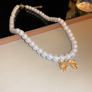 Dettaglio di una collana di perle bianche con ciondolo a fiocco dorato su base in pelle