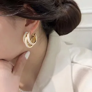 Modern gold-plated C-shaped layered earrings with white enamel worn by a model