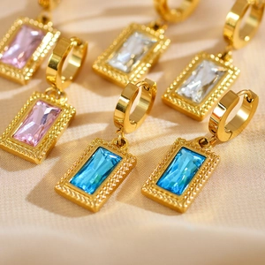Detail of gold rectangular geometric earrings with pink and blue zircons on silk fabric