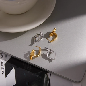 Polished minimalist 18K gold and silver twisted hoop earrings on urban lifestyle background