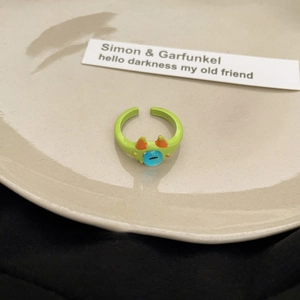 Detail of green enamel cartoon open ring featuring a blue eye charm on a ceramic tray