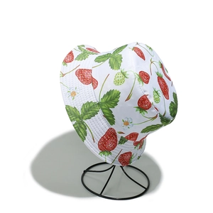 Detail of white bucket hat with vibrant red strawberry and floral patterns on wire stand