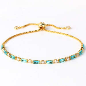 Detailed shot of a gold bracelet featuring blue baguette stones and clear round crystals