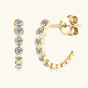 Detail view of golden C-shaped earrings inlaid with sparkling round zircon stones
