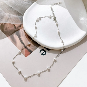 Detailed close-up of a vintage pearl choker necklace with silver chain on a white tray