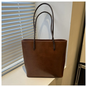 Detail of deep brown tote bag with slim straps against a minimalist window background