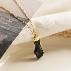 Gold minimalist necklace with black drop oil fist pendant on a warm textured background