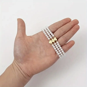 Detailed view of three pearl bracelets with golden heart charms engraved with letters A, M, R