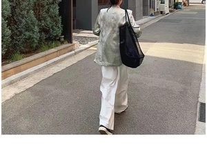 Detail of a black mesh tote bag paired with silver textured jacket and white pants