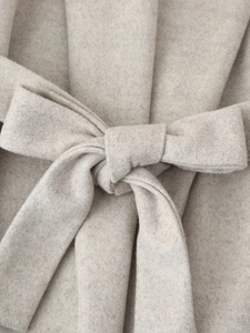 Close-up of the elegant bow-tie waist belt on a light gray wool coat fabric detail