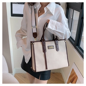 Canvas tote bag with brown leather trim and wide strap shown on a model in bright light